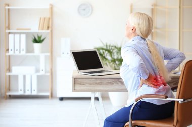 Mature businesswoman suffering from back pain in office