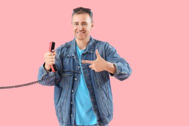 Olgun bir adam pembe arkaplanda telefon ahizesini işaret ediyor.