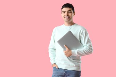 Pembe arka planda dizüstü bilgisayarı olan mutlu genç adam.