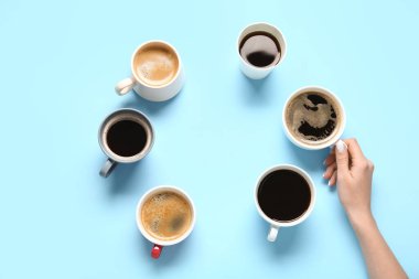 Mavi arka planda sıcak kahve fincanları olan kadın eli çerçevesi.