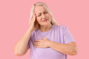 Pembe arka planda göğüs ağrısı çeken olgun bir kadın. Kanser farkındalığı kavramı