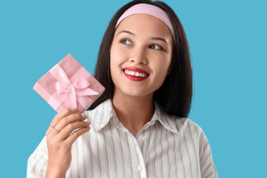 Mavi arka planda hediye kutusu olan güzel bir Asyalı kadın.