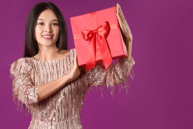 Mor arka planda hediye kutusu olan güzel bir Asyalı kadın.