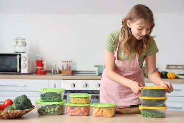 Güzel genç bir kadın ve mutfaktaki masada dondurmak için sebzeli plastik kaplar.