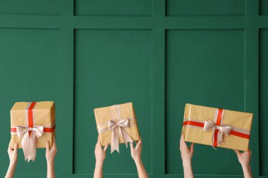 Yeşil arka planda Noel hediyesi kutularını tutan kadın eller