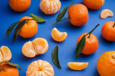 Tasty tangerines with leaves on blue background