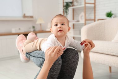 Küçük bebeğiyle evde yoga yapan genç ve güzel bir kadın.