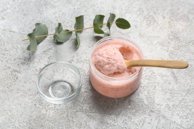 Bir kavanoz vücut fırçası, cam kase ve arka planda okaliptüs dalı.