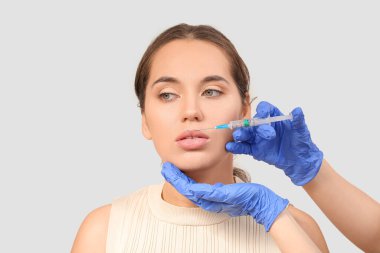 Gri arka planda dudak enjeksiyonu alan güzel bir kadın.