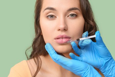 Yeşil arka planda dudak enjeksiyonu gören genç bir kadın, yakın plan.