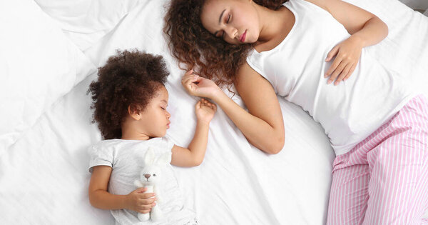 Little African-American girl with mother sleeping in bed