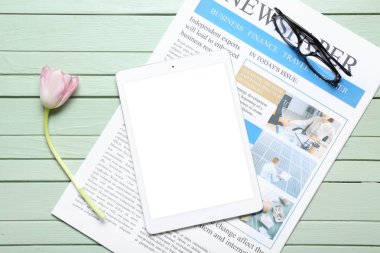 Tabletli gazete, lale çiçeği ve yeşil ahşap arka planda gözlük.