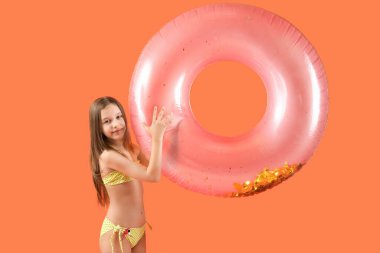 Turuncu arka planda şişirilebilir yüzüğü olan mayo giymiş şirin küçük bir kız.