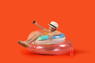 Şortlu, şapkalı, cep telefonu olan ve turuncu arka planda selfie çeken Afro-Amerikalı bir çocuk.