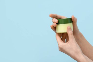 Mavi arka planda yüz kremi kavanozu olan kadın elleri