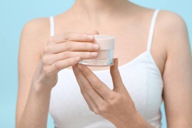 Mavi arka planda bir kavanoz yüz kremi ile güzel genç bayan, yakın plan