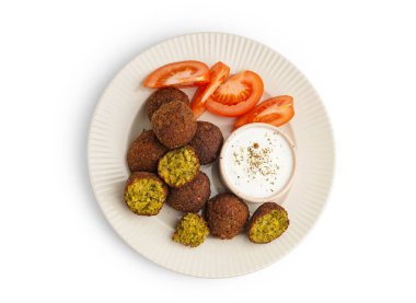 Beyaz arka planda nefis falafel topları, sos ve domates tabağı.