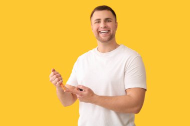 Handsome young happy diabetic man using lancet pen on yellow background clipart