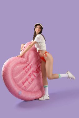 Plaj elbisesi içinde güzel bir kadın kalp şeklinde yüzme yatağı ve leylak arkaplanı var.