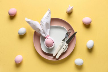 Sarı arka planda boyanmış yumurtalarla Paskalya kutlaması için masa ayarlayın. Üst görünüm