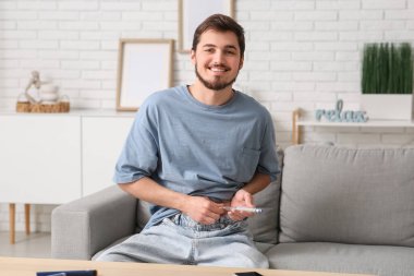 Şeker hastası genç adam evdeki kanepede tükenmez kalem kullanıyor.