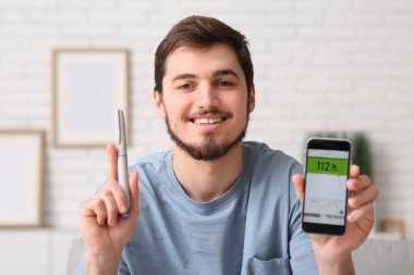 Evde kan şekerini ölçen cep telefonu ve tükenmez kalemli diyabetik genç adam, yakın plan.