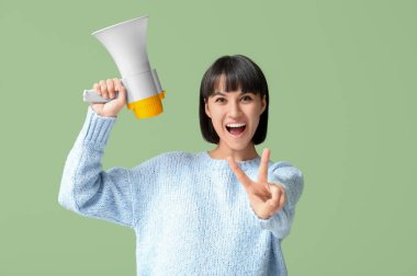Megafonlu genç kadın yeşil arka planda zafer jesti gösteriyor.