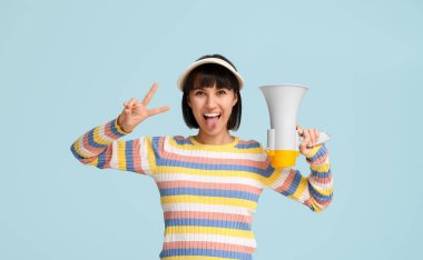 Mavi arka planda zafer jesti gösteren megafonlu genç bir kadın.