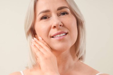 Bej arka planda sağlıklı ciltli, güzel, olgun, mutlu bir kadın.