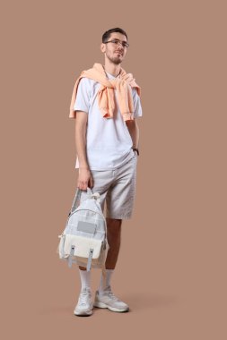 Gözlüklü ve sırt çantalı şık elbiseli yakışıklı genç adam bej arka planda poz veriyor.