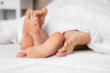 Yatakta battaniyenin altında yatan genç çiftin çıplak ayakları