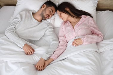 Genç çift uyuyor ve yatakta el ele tutuşuyorlar.