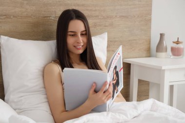 Dergi taşıyan genç bir kadın yatakta yatıyor.