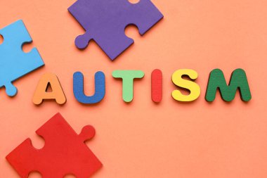 Kelime AUTISM ve turuncu arka planda renkli yapboz parçaları. Üst görünüm