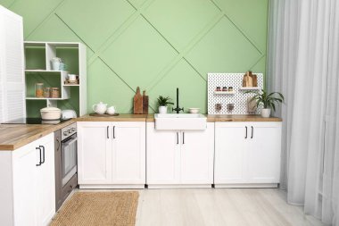 Beyaz tezgahlı, tahta tahtalı ve yeşil duvarlı şık bir mutfak.