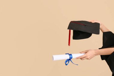 Diplomalı kadın eller ve bej arka planda mezuniyet şapkası.