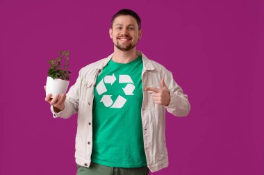 Geri dönüşüm logosu pembe arka plandaki bitkiyi gösteren tişörtlü mutlu genç adam. Ekoloji kavramı