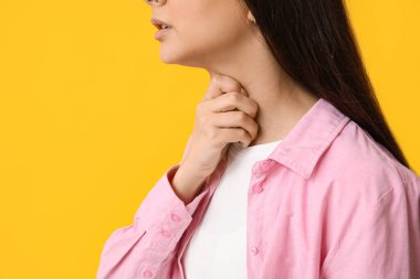 Sarı arka planda boğazı ağrıyan genç bir kadın, yakın plan.