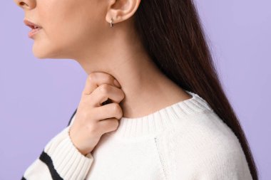 Leylak arka planında boğaz ağrısı çeken genç bir kadın, yakın plan.