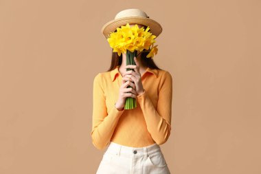 Bej arka planda güzel narsisli çiçeklerle dolu buketi olan güzel genç bir kadın.