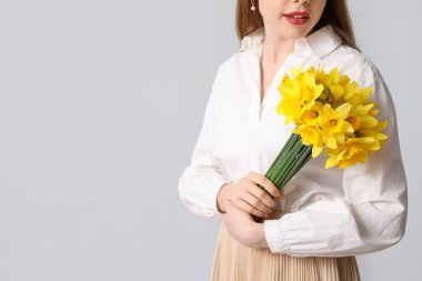 Gri arka planda bir buket güzel nergis çiçeğiyle genç bir kadın.