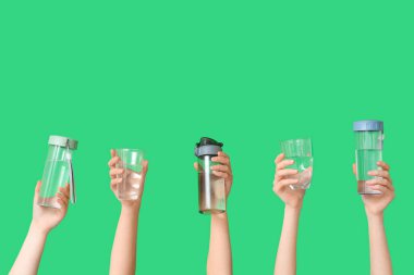Farklı bardaklara ve yeşil arka planda su şişelerine sahip kadın elleri.