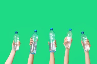 Yeşil arka planda farklı su şişeleri olan kadın eller.