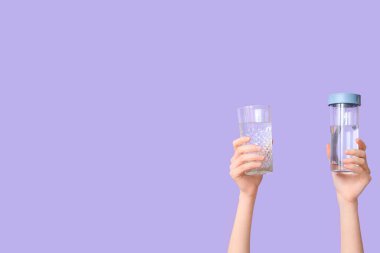 Cam ve su şişesiyle leylak arka planda olan kadın eller, yakın plan.