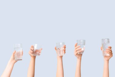 Gri arka planda farklı su bardakları olan kadın eller.