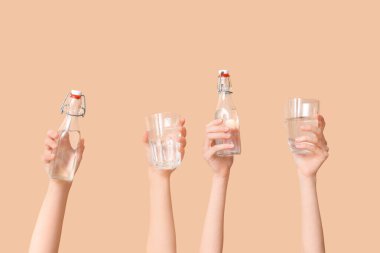 Renkli arka planda şişe ve bardak su taşıyan kadın eller, yakın plan.