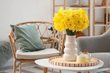 Oturma odası, koltuk, sehpa ve vazo dolusu narsisli çiçekler.