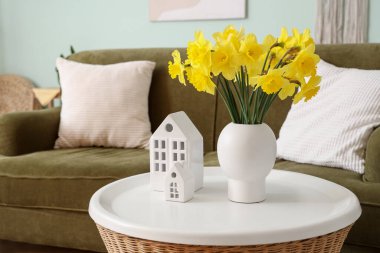 Sehpanın üzerinde narsis çiçekleri olan vazo. Oturma odasındaki rahat kanepenin yanında. Yakın çekim.