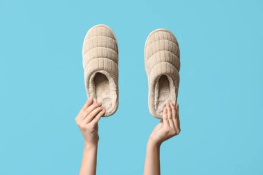 Mavi arka planda bir çift terliği tutan kadın el.