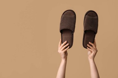 Bej arka planda kahverengi terlikleri tutan kadın eller.